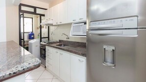A modern kitchen with white cabinets, a stainless steel refrigerator, a built-in microwave, and a granite countertop. - Cayman 123 - Apto 80M Praia de Bombas (Bombinhas)