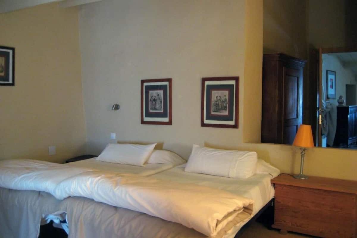 Ein Hotelzimmer mit zwei Betten, einem Holfnachtkästchen, einer Lampe und zwei gerahmten Bildern an der Wand.