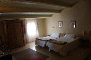 A room with two single beds, a wooden wardrobe, a small table, and a nightstand with a lamp. - Casa rural La Cantarera (Herguijuela)