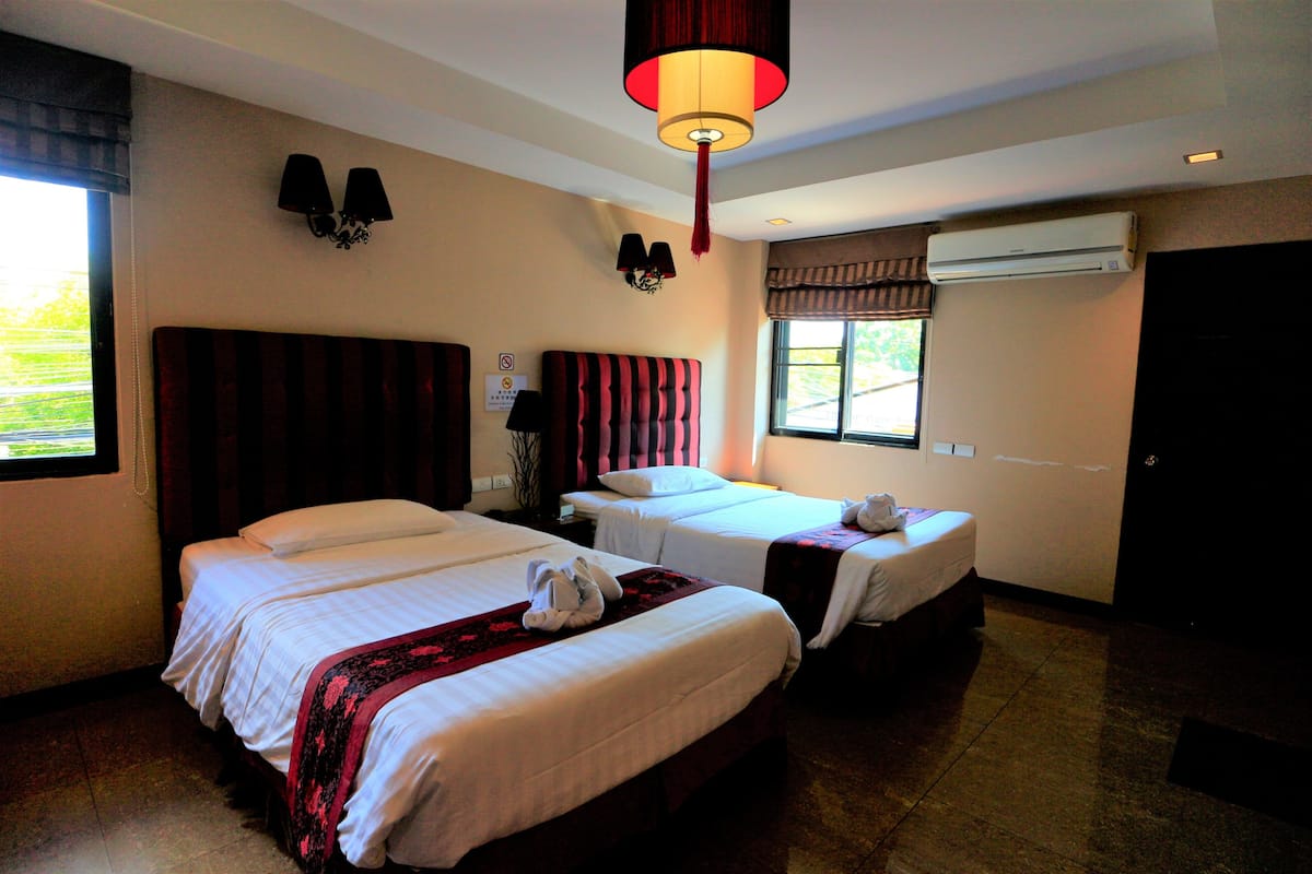 A hotel room with two beds, a large window, an air conditioning unit, and a red hanging lamp.