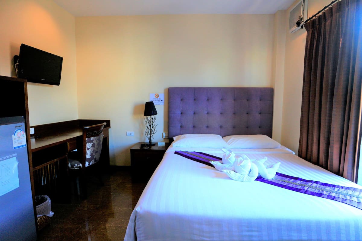A hotel room with a bed, a television on the wall, a nightstand, and a desk with a chair.