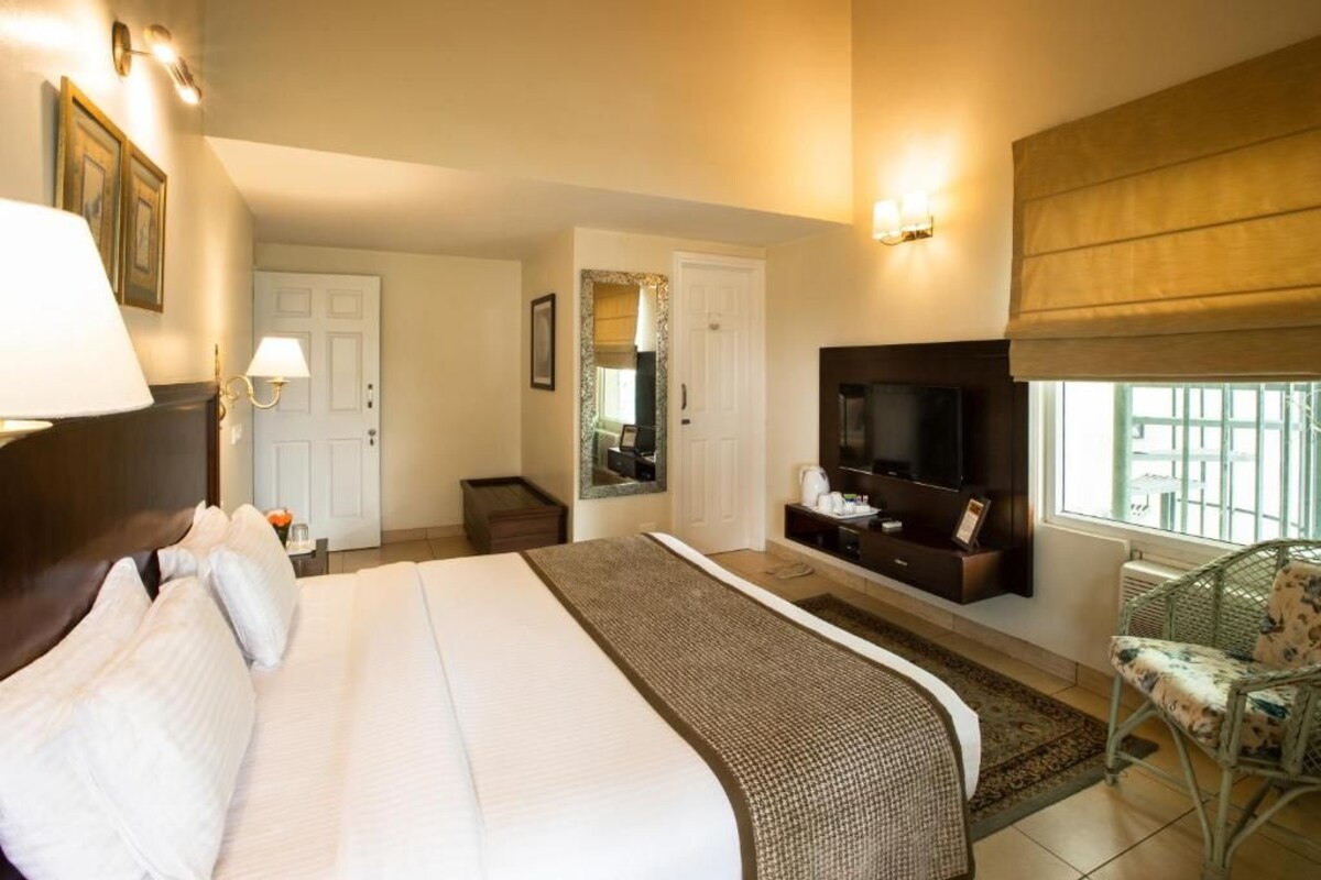 A hotel room with a large bed, a television, a seating area with a chair, and a window with a view.