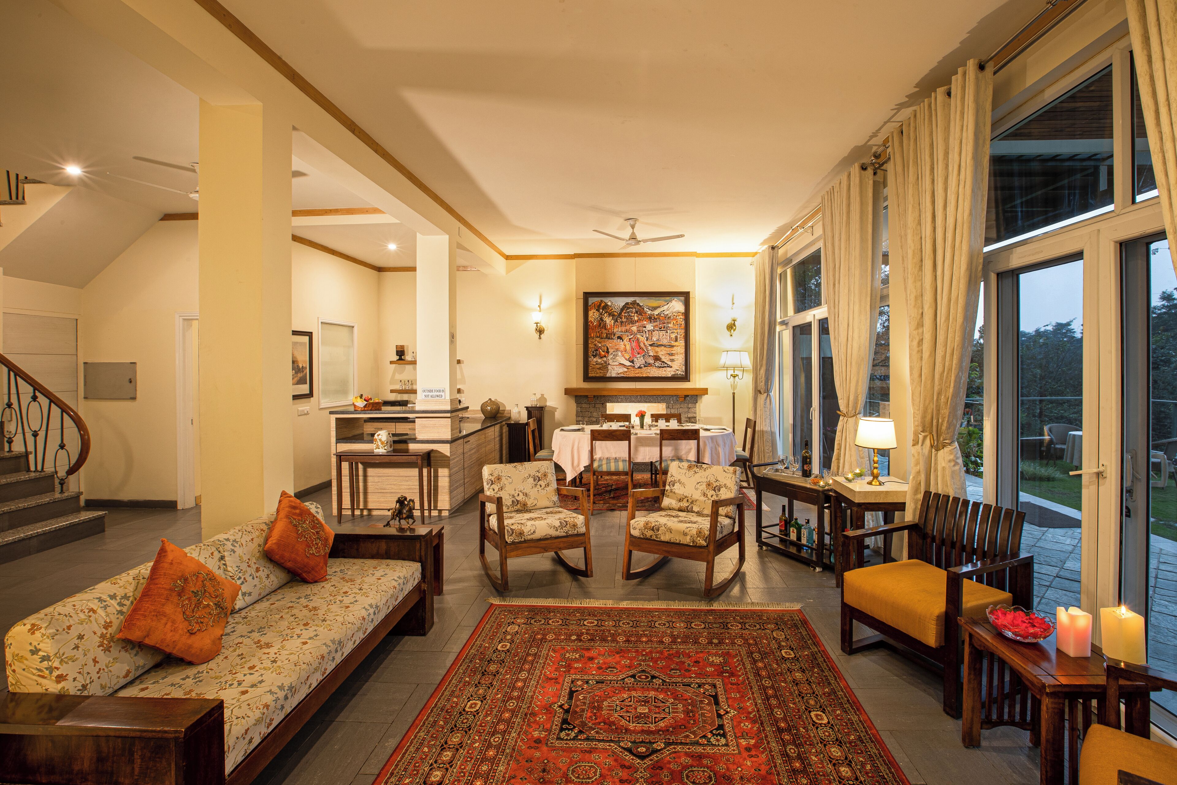 A spacious living area with a sofa, chairs, a dining table, and a view through large windows.