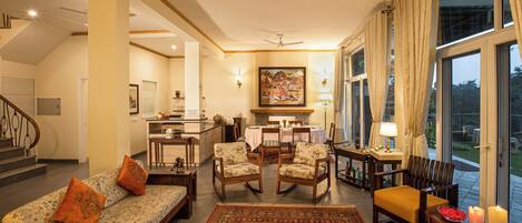A spacious living area with a sofa, chairs, a dining table, and a view through large windows.