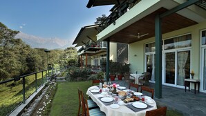 An outdoor dining area with a table set for four, surrounded by chairs, with a mountain view in the background. - Lamrin Norwood Green Palampur (Palampur)