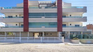 Un immeuble à plusieurs étages, doté d’une colonne rouge centrale, de balcons et d’une entrée ferm ée par un portail.