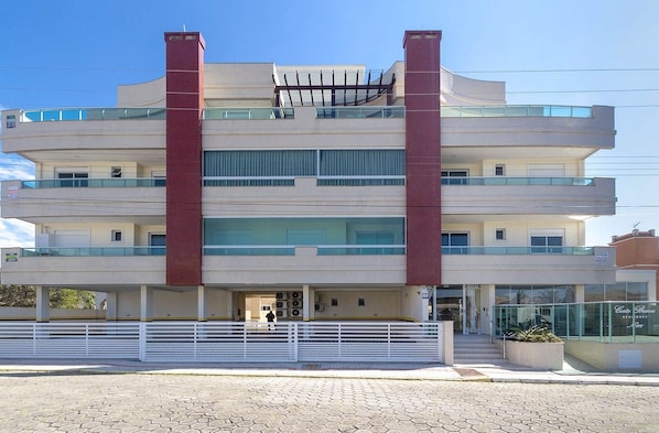 A multi-story building with a central red column, balconies, and a gated entrance.