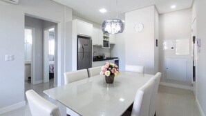 Une cuisine moderne avec des meubles blancs, un réfrigérateur et un four à micro-ondes. On y trouve une table à manger avec des chaises et un vase rempli de fleurs.