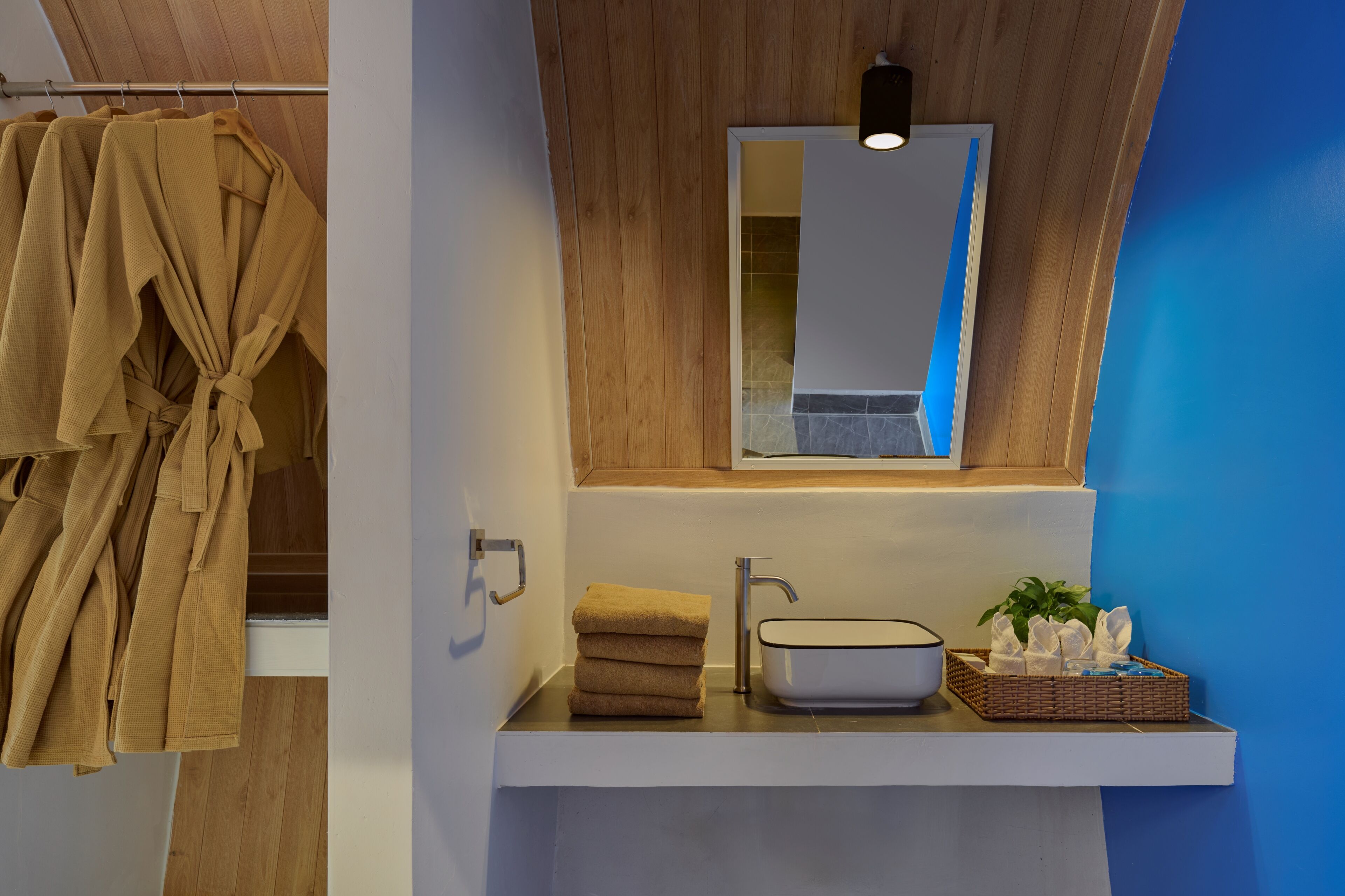 Une salle de bain avec un meuble-lavabo en bois, un évier, un miroir et un porte-serviettes avec des peignoirs.