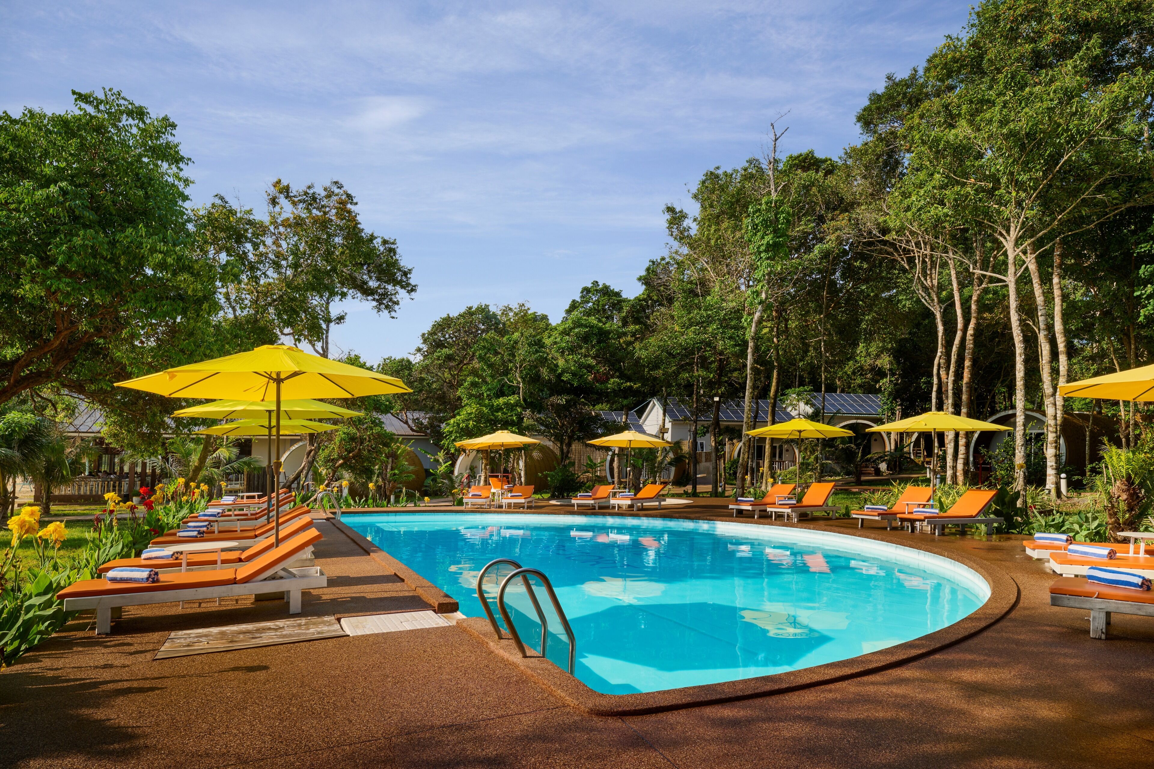 A pool area with lounge chairs and umbrellas, surrounded by trees.