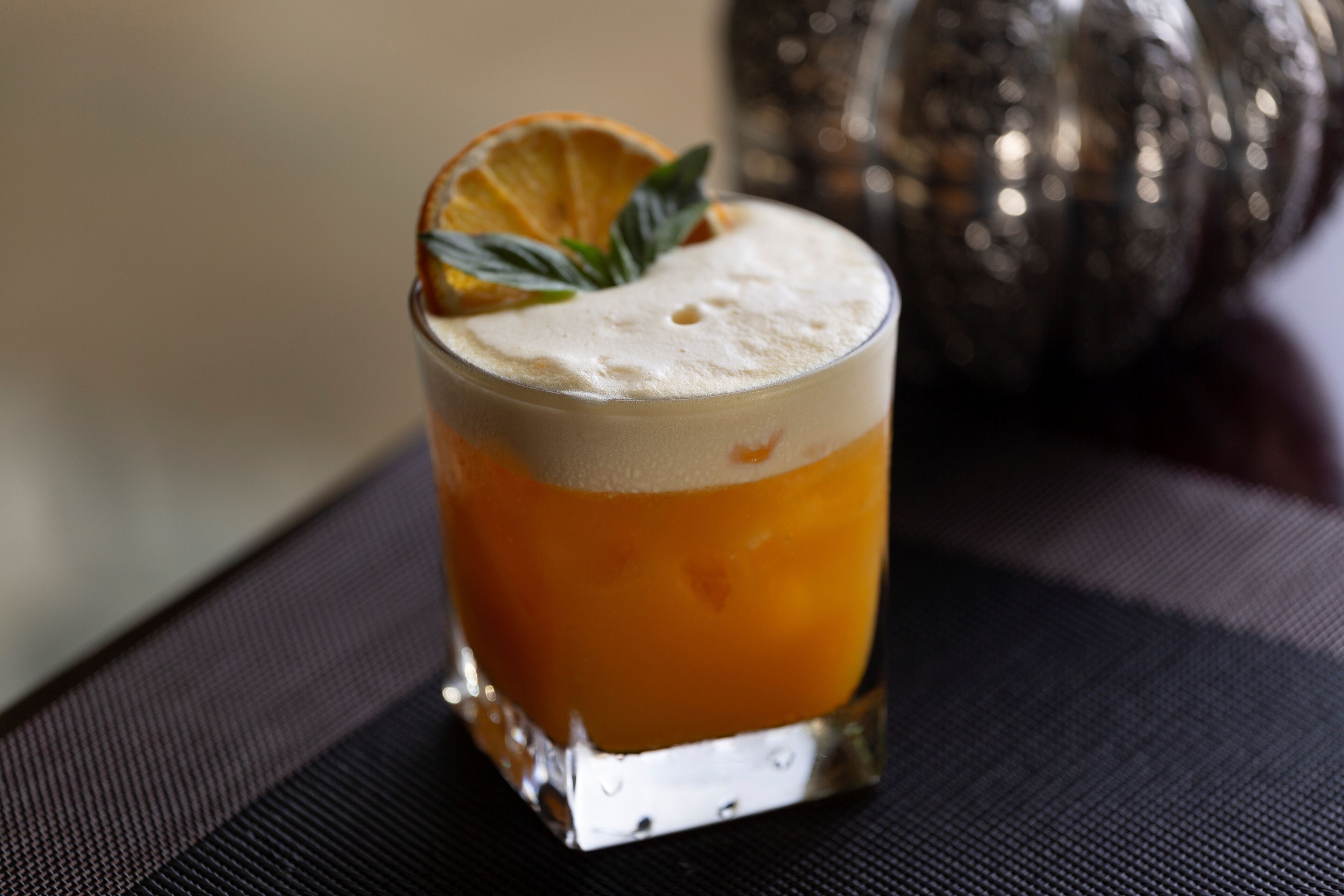 Un verre d’une boisson orangée, agrémentée d’une garniture, posé sur une surface texturée.