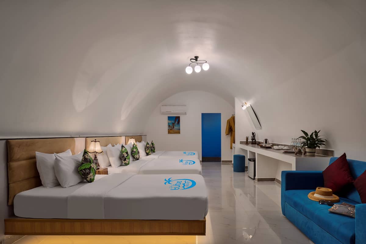 A modern hotel room with a large bed, a blue sofa, a desk, and a kitchen area.