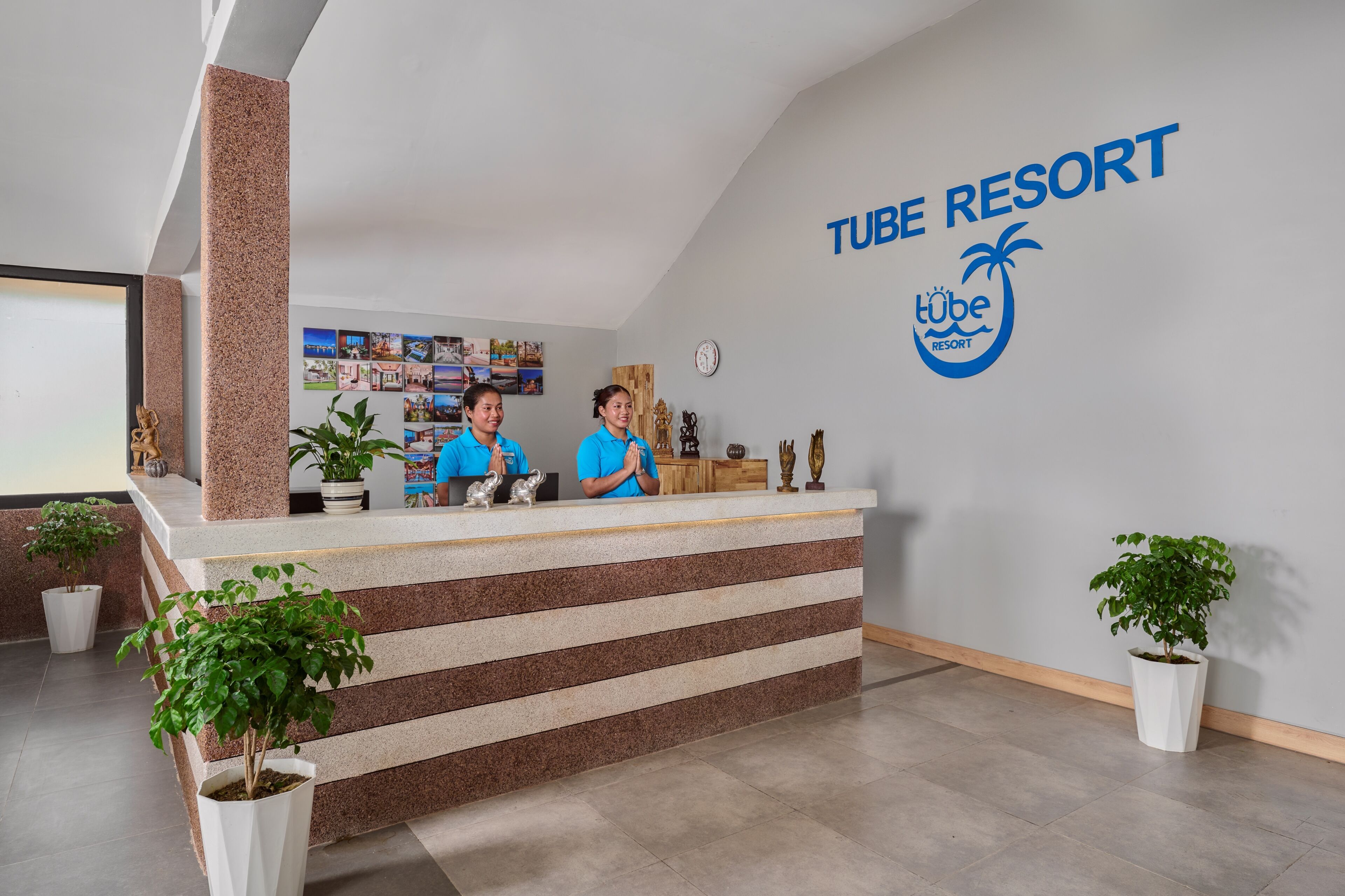 Un comptoir d’accueil avec deux employés, une horloge et un mur orné du logo de Tube Resort.