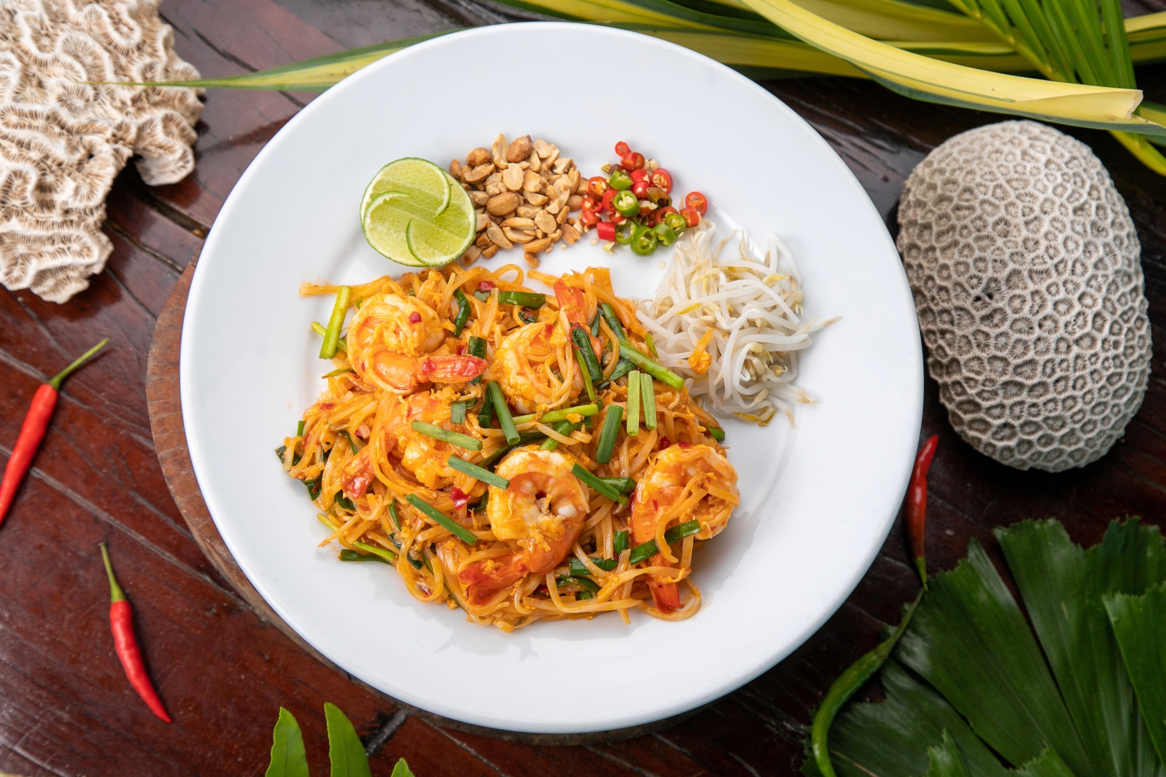 A plate of Pad Thai with shrimp, bean sprouts, peanuts, and lime.