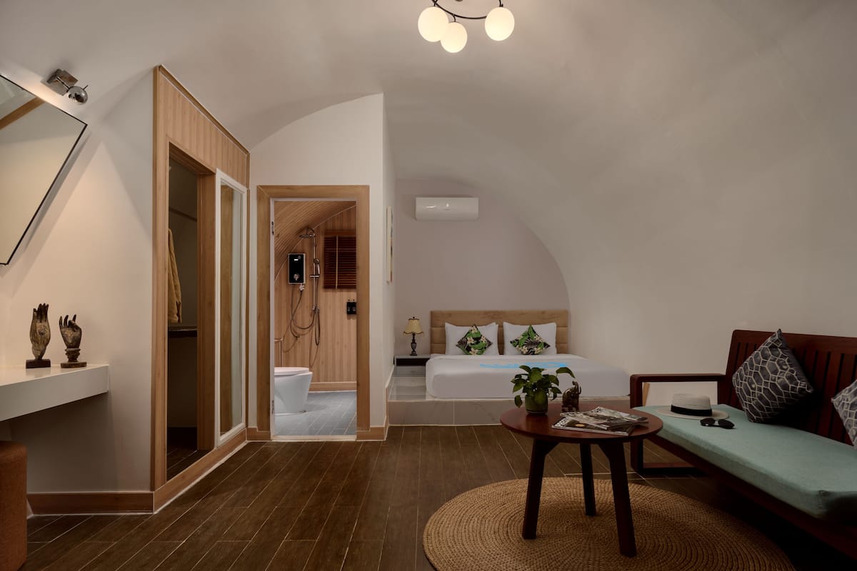 A modern room with a bed, a sofa, a small table, and a shower area.