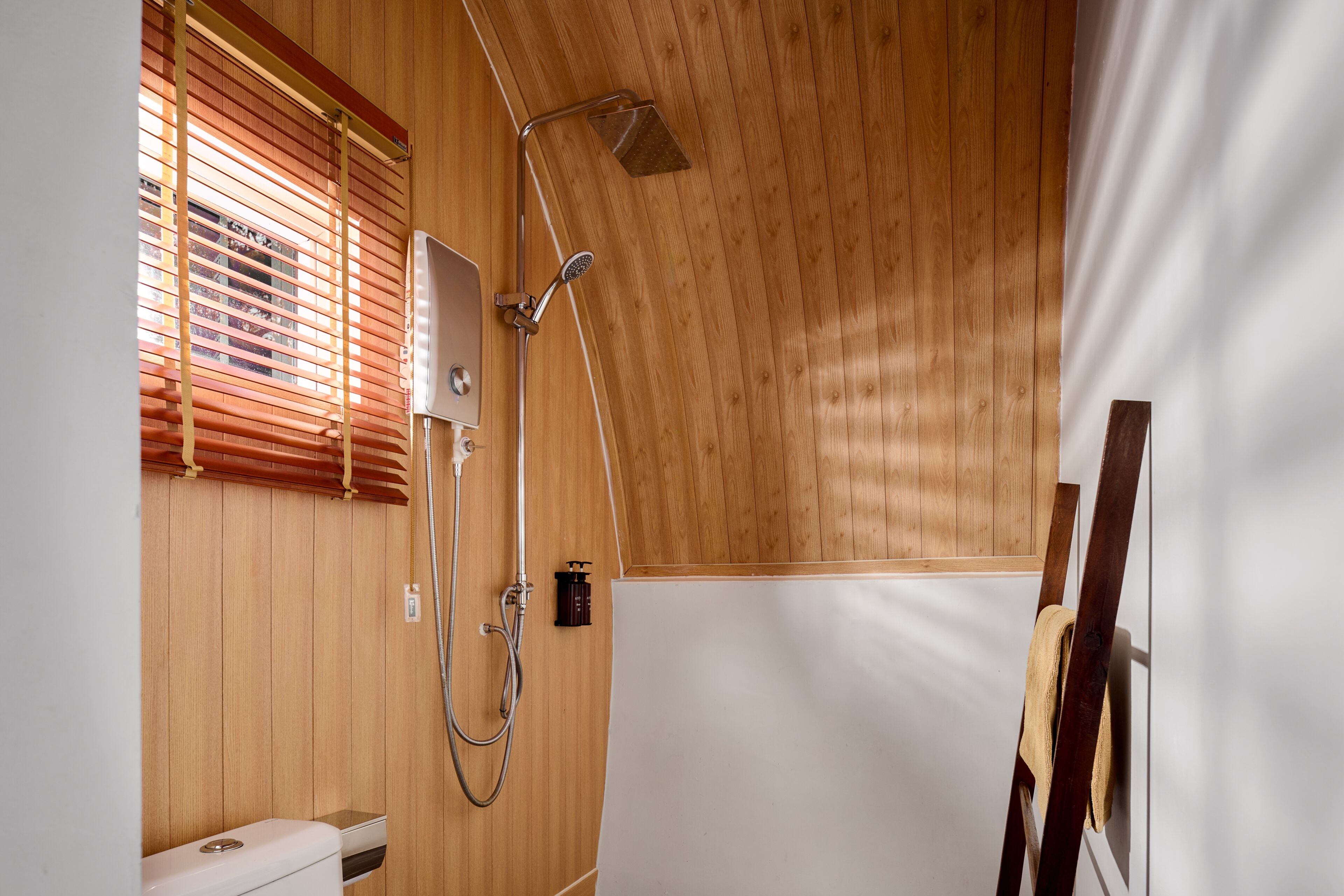 Une salle de bain aux murs lambrissés, équipée d’une douche, de toilettes et d’un porte-serviettes.