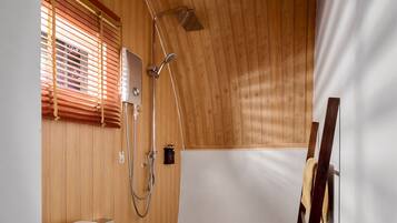 Une salle de bain aux murs lambrissés, équipée d’une douche, de toilettes et d’un porte-serviettes.