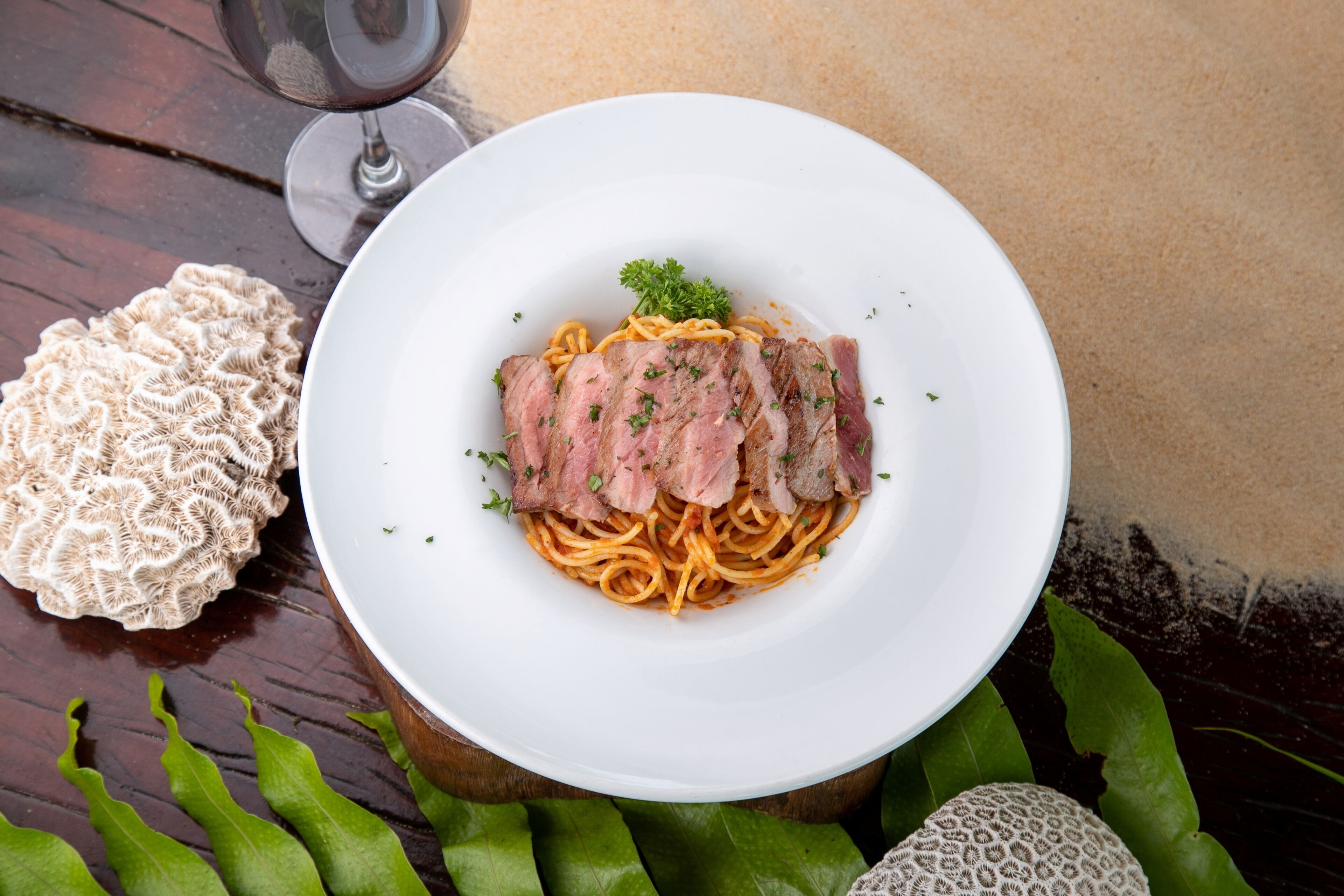 A plate of pasta with meat and herbs, a glass of wine, and decorative items on a wooden table.