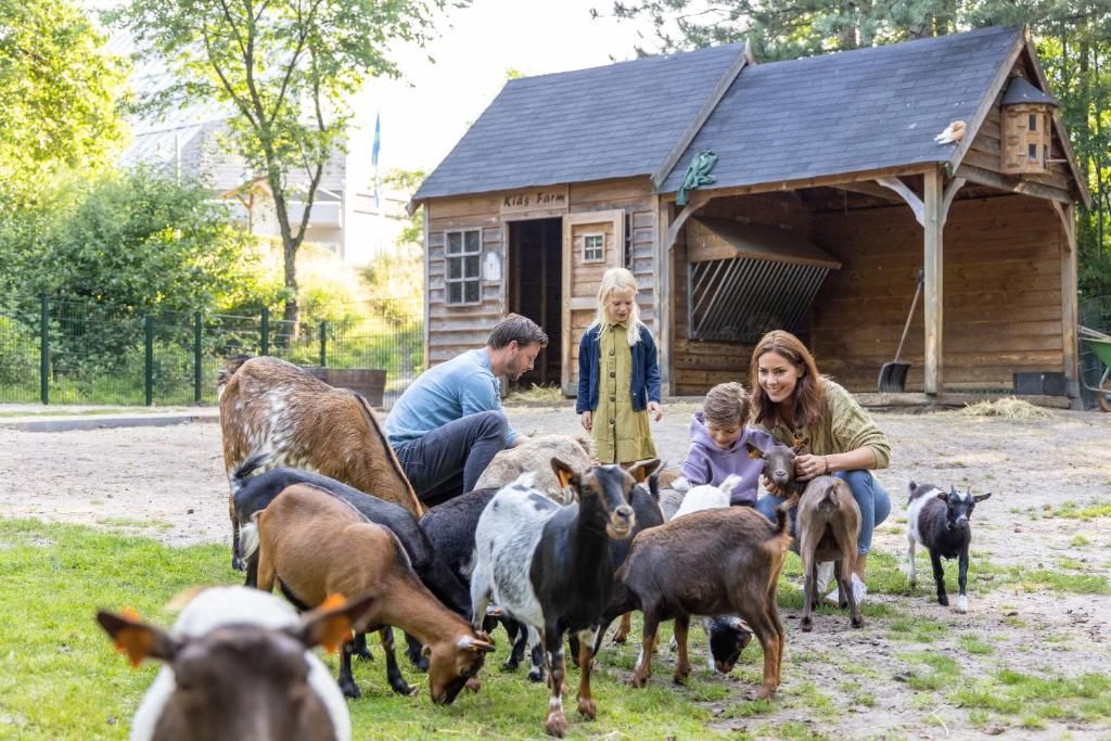A rustic wooden building labeled 'Kids Farm' with a thatched roof, surrounded by a group of people and various farm animals.