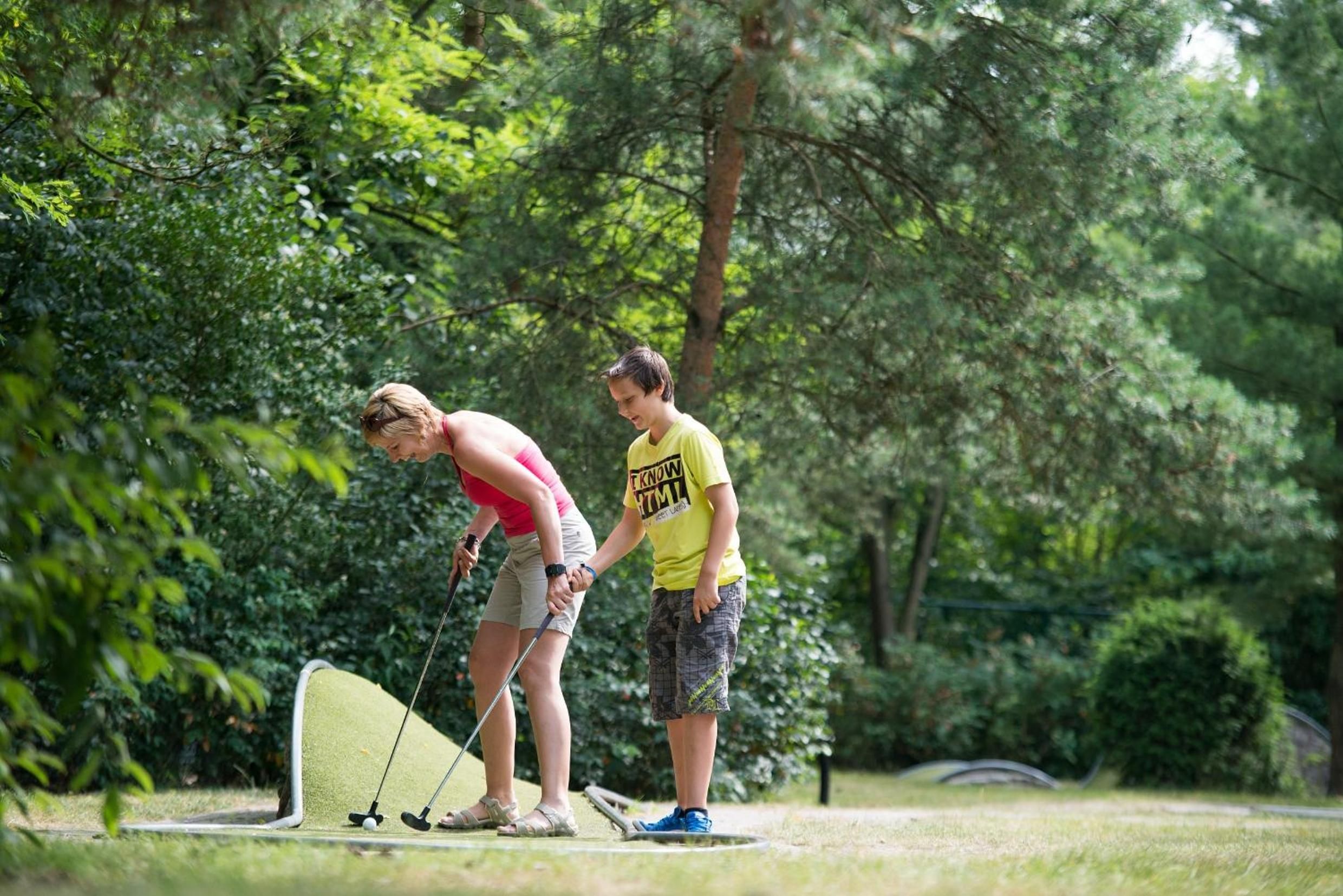 Dos personas jugando golf en un parque con árboles de fondo.