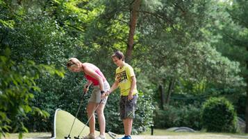 Dos personas jugando golf en un parque con árboles de fondo.