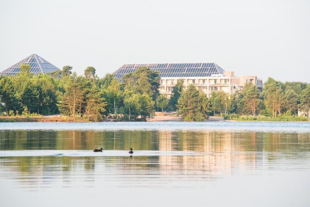 A building with a modern design, a body of water in the foreground, and trees in the background.