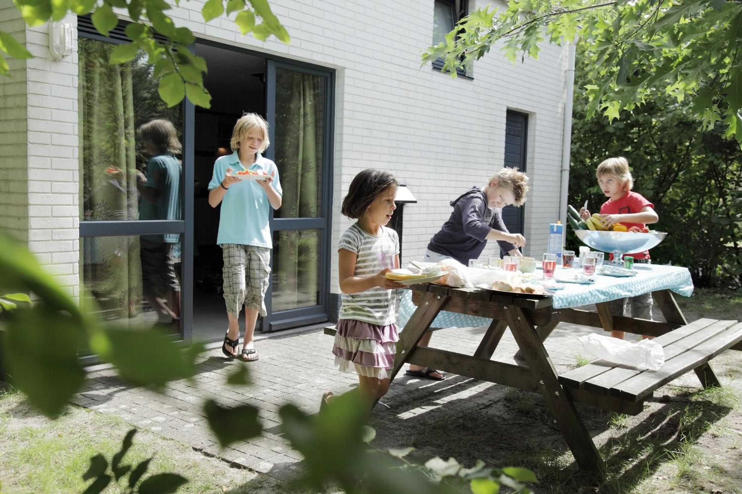 Une terrasse en bois avec une table de pique-nique, située à l’extérieur d’une maison dotée de grandes fenêtres.