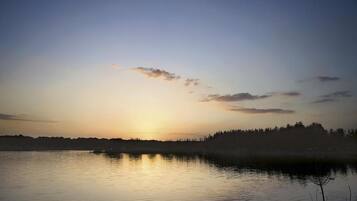 Um lago calmo ao amanhecer, com silhuetas de árvores ao fundo.