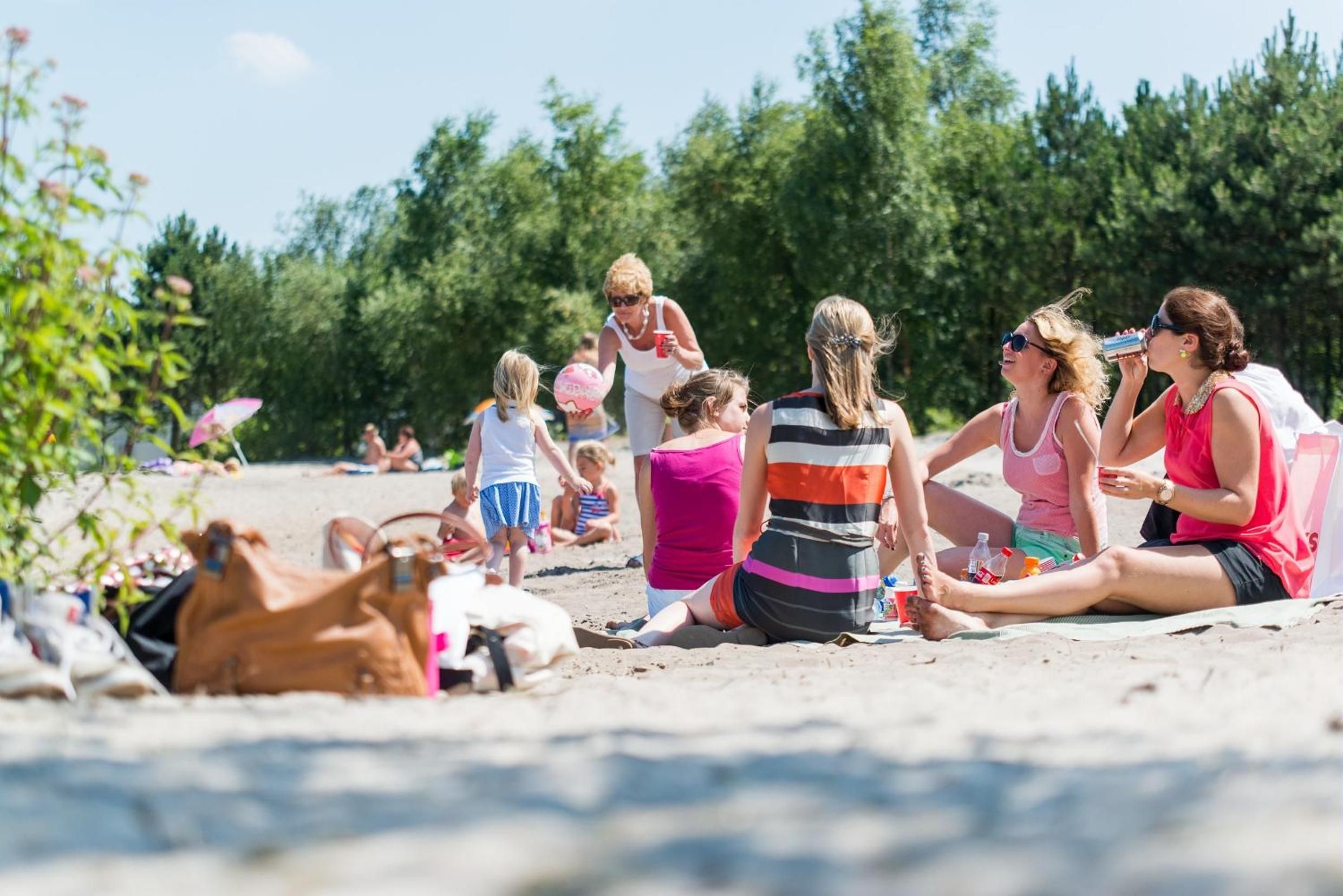 Een groep mensen zit op een zandstrand, met bomen op de achtergrond.