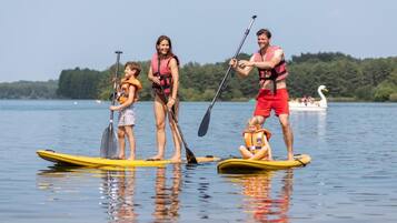 Un grupo de personas en tablas de paddleboard en un lago tranquilo, con un bote al fondo.