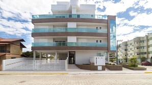 A multi-story residential building with a modern design, featuring balconies, a gated entrance, and a paved driveway. - Costa Dourada 204 - Apto Praia Mariscal (Bombinhas)