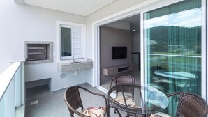 A balcony with wicker chairs, a TV, and a stone fireplace. - Costa Dourada 204 - Apto Praia Mariscal (Bombinhas)