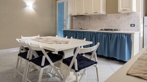 A compact kitchen with white cabinets, a blue countertop, and a dining area with a white table and chairs. - B&B De Sire (Agnone)