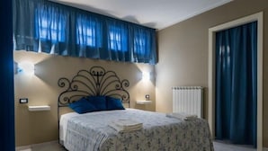 A bedroom with a bed, two bedside tables, a radiator, and a window with curtains. - B&B De Sire (Agnone)
