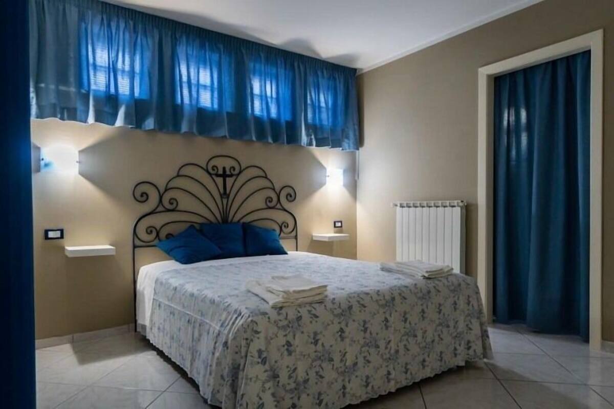 A bedroom with a bed, two bedside tables, a radiator, and a window with curtains.
