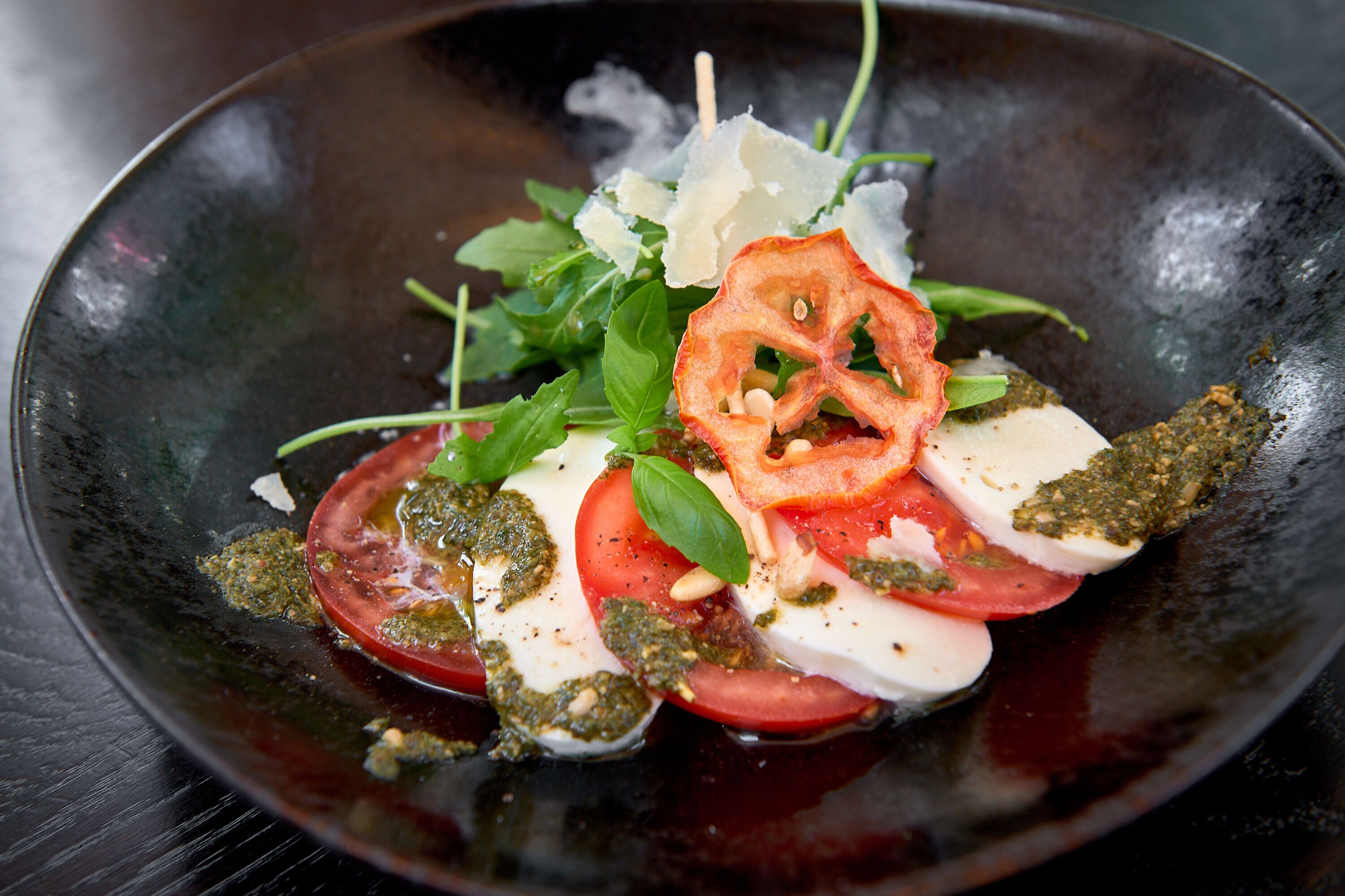 Ein Gericht mit Tomaten, Basilikum und Käse auf einem dunklen Teller.