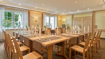 Un comedor con largas mesas de madera dispuestas para varios invitados, con velas y cristalería.