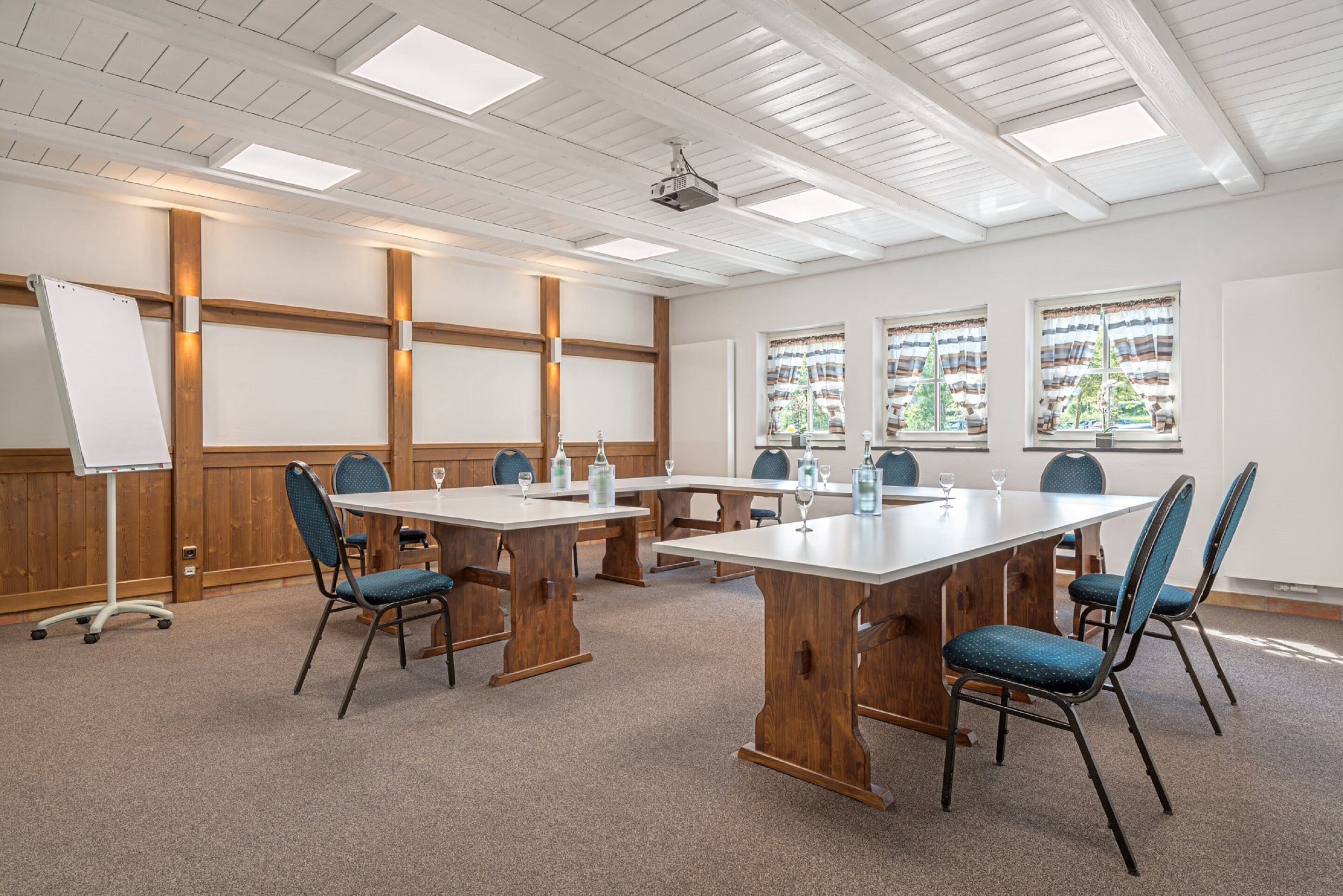 Une salle de conférence équipée d’une grande table, de chaises, d’un tableau blanc et de fenêtres avec des rideaux.