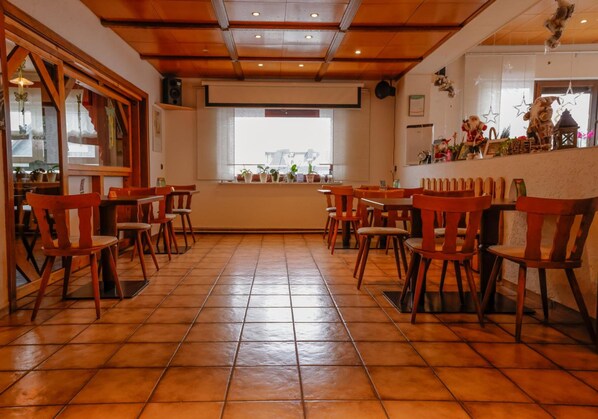 A restaurant interior with wooden chairs and tables, a tiled floor, and a large window with a view.