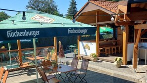 Un espace extérieur aménagé avec des tables et des chaises, une terrasse couverte dotée d’un toit végétalisé et une structure en bois surmontée d’un toit en tuiles.