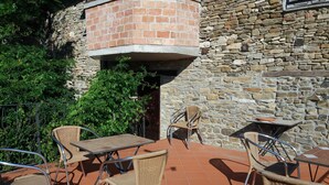 Une terrasse extérieure avec des chaises et des tables en osier, un mur en pierre et une structure en briques.