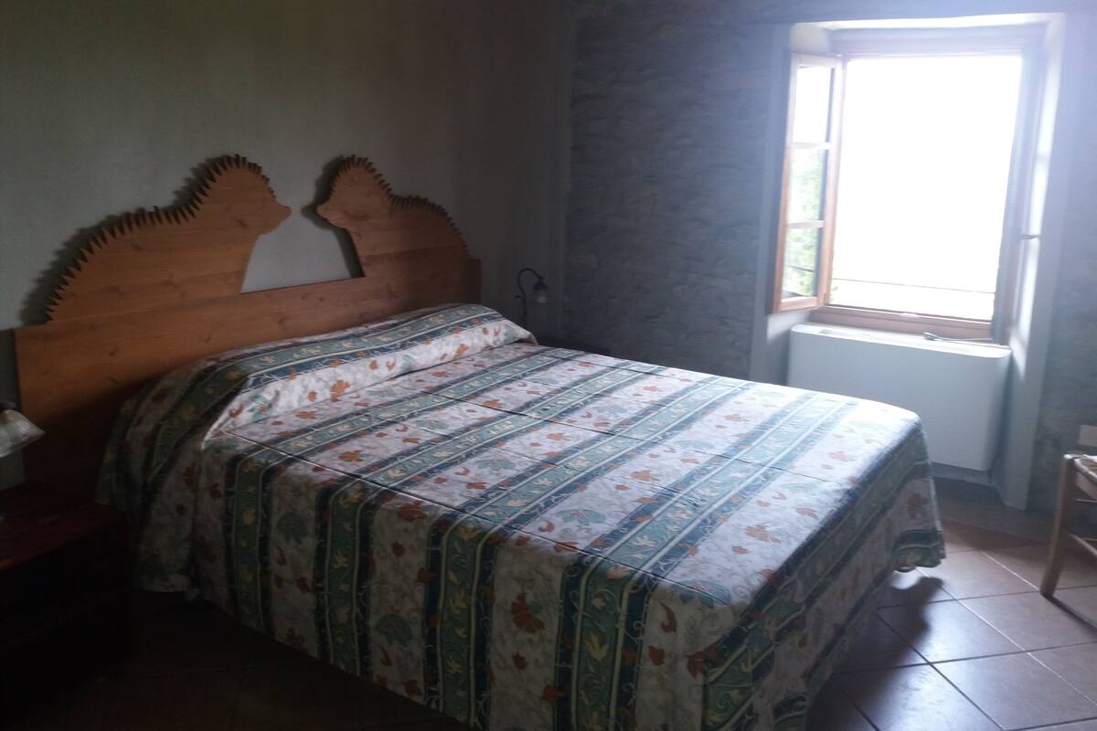 A bedroom with a wooden headboard, a patterned bedspread, and a window with a view of greenery.