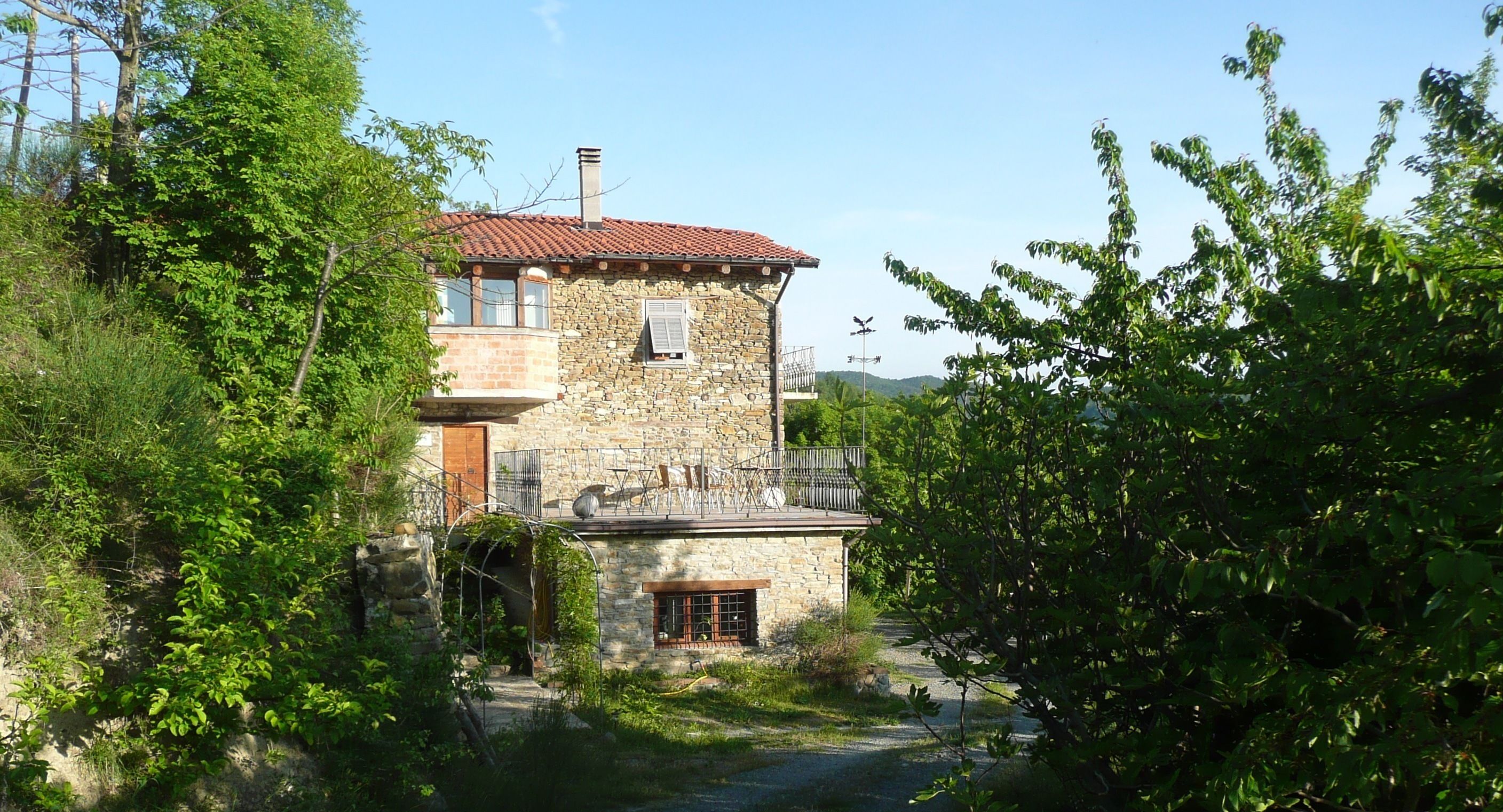 Une maison en pierre avec un toit recouvert de tuiles rouges, un balcon et une petite fenêtre.
