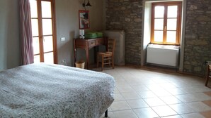 Une chambre à coucher avec un lit, un bureau, une chaise, une fenêtre et un mur en pierre.