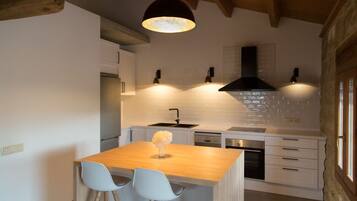 A modern kitchen with a wooden island, two bar stools, a black range hood, and pendant lighting.