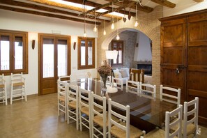 Un comedor con una mesa de vidrio rodeada de sillas blancas, una chimenea y puertas de madera.