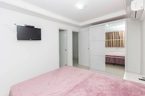 A bedroom with a bed, a TV mounted on the wall, a wardrobe, and a window with curtains.