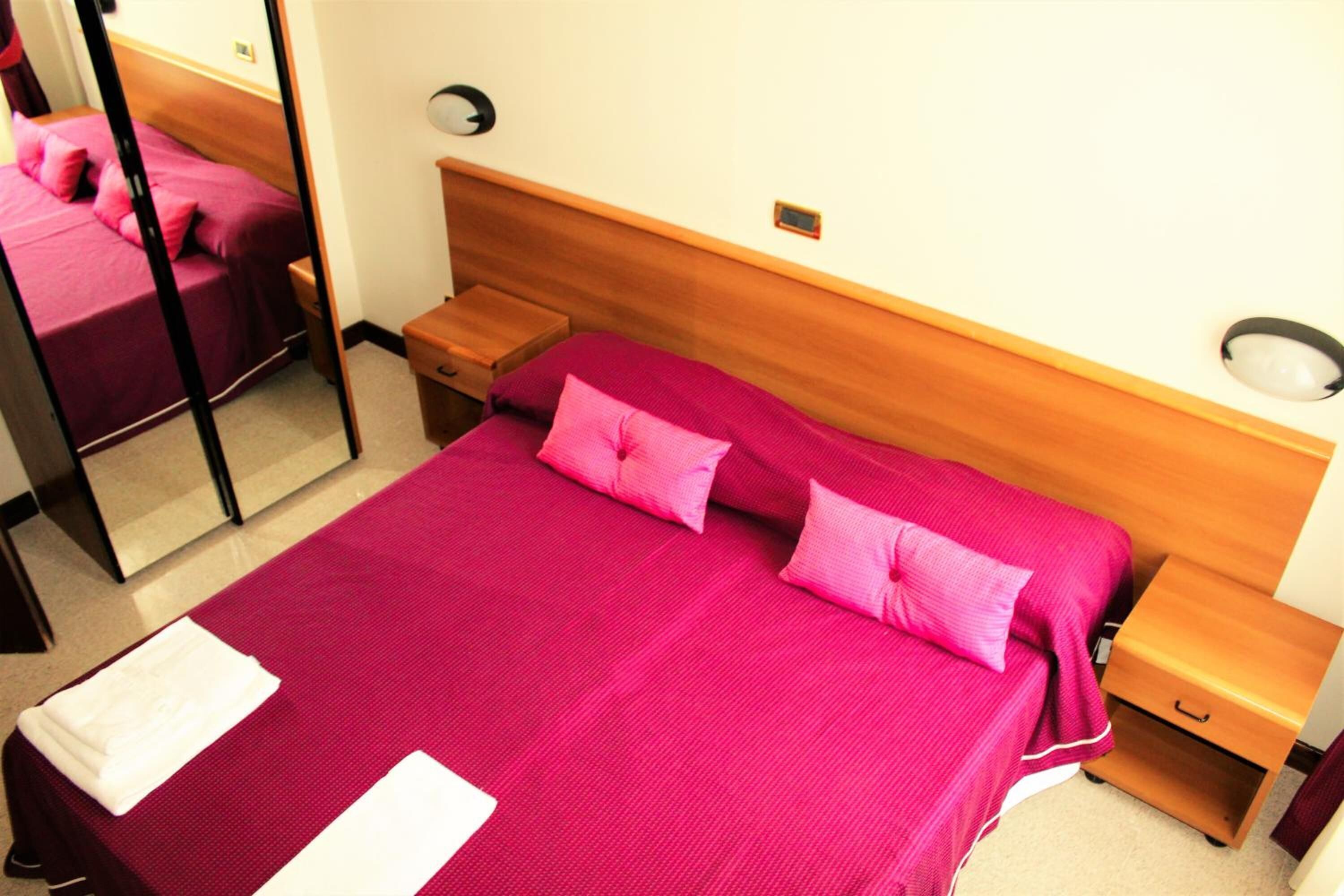 A hotel room with a large bed, wooden headboard, bedside tables, and a mirror.
