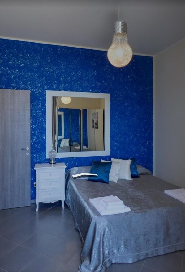 A bedroom with a large bed, a dresser, a mirror, and a hanging light fixture. - Il Postiglione (Minturno)