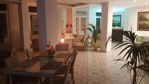 A dining area with a glass table and chairs, a decorative wall, and a potted plant. - Klaton Beach Hotel (Formia)